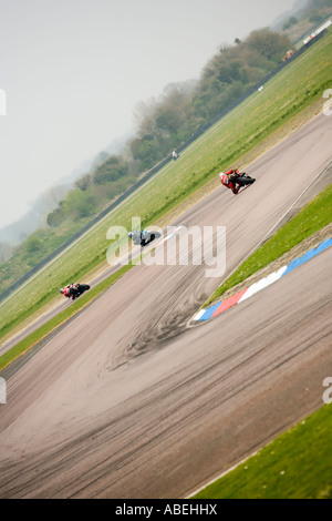 three racing motorbikes chasing, riders leaning through corners Stock Photo