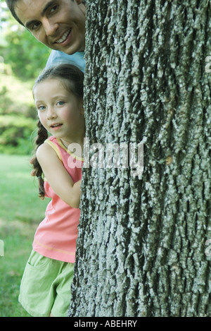 Girl and father peeking around tree trunk Stock Photo