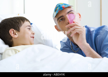 Intern next to boy in hospital bed, wearing mask and blowing party horn