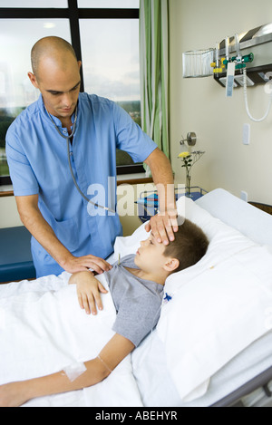 Boy lying in hospital bed, intern taking his temperature Stock Photo