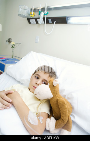 Boy lying in hospital bed next to stuffed animal Stock Photo