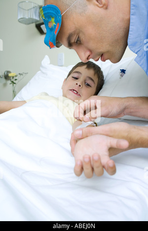 Boy lying in hospital bed, intern wearing mask on head removing adhesive tape from boy's arm