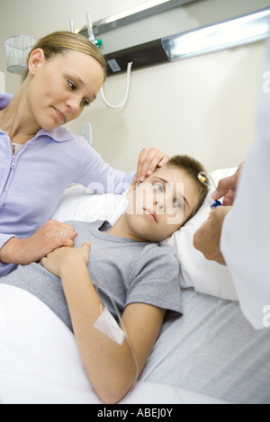Boy lying in hospital bed, mother sitting by side while doctor holds IV tube Stock Photo