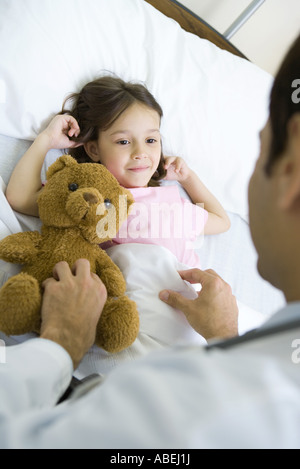 Girl lying in hospital bed, smiling up at doctor