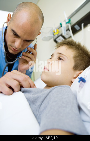 Boy lying in hospital bed, intern listening to boy's chest with stethoscope Stock Photo