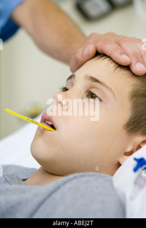 Boy with thermometer in mouth and man's hand on forehead Stock Photo