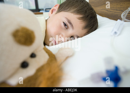 Boy lying in hospital bed, looking at camera through half closed eyes Stock Photo