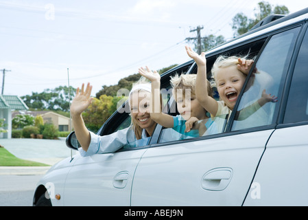 Mother and two children waving out of car windows, looking at camera Stock Photo