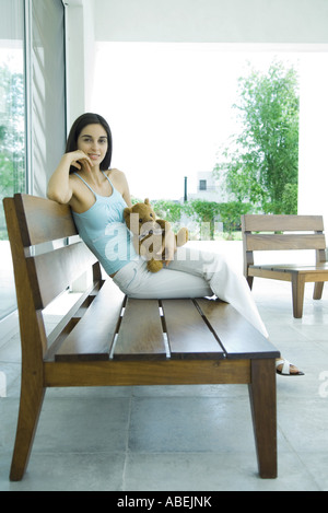 Woman sitting on patio furniture holding teddy bear, full length Stock Photo