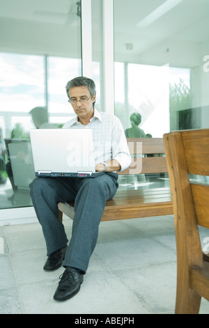 Man sitting, using laptop on patio, full length Stock Photo