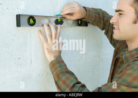 Man using level to draw line on wall Stock Photo