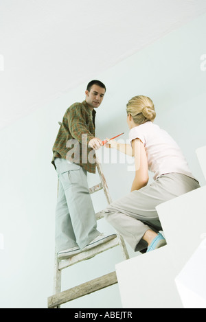 Man on ladder handing woman screwdriver Stock Photo