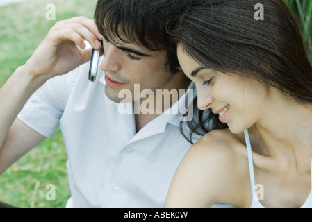 Young couple sitting close together, man using cell phone Stock Photo