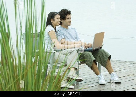 Couple sitting on dock using laptop Stock Photo