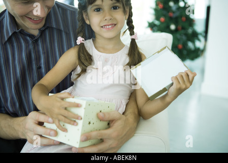 Girl sitting on father's lap holding Christmas present Stock Photo