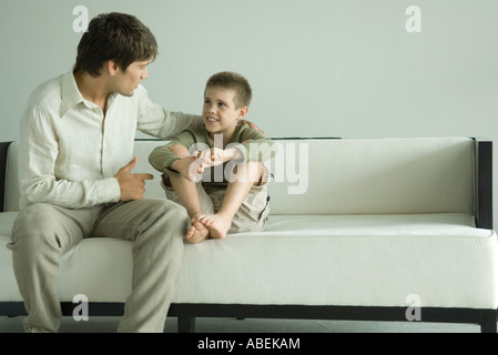 Father and son sitting on sofa, talking Stock Photo