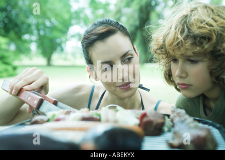 Boy looking at meats cooking on barbecue, woman glancing at him Stock Photo