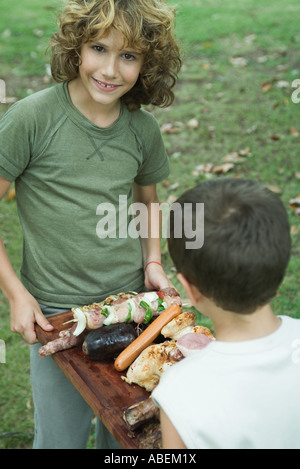 Two boys carrying tray of grilled meat Stock Photo