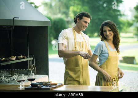 Man tying woman's apron by outside wood oven Stock Photo