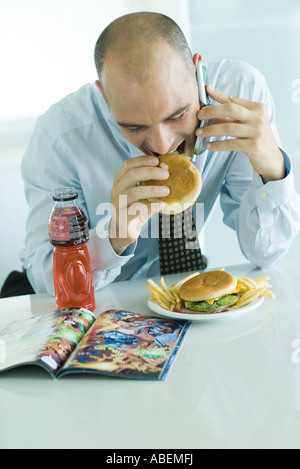 Man eating hamburgers, using cell phone, and looking at comic book