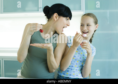 Girl holding ice cream dessert, next to woman holding cherry, woman leaning toward girl with mouth wide open Stock Photo