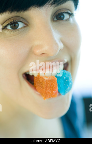 Woman holding pieces of candy between teeth, smiling at camera Stock Photo