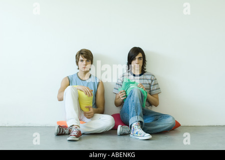 Two teen boys sitting on floor, holding cushions Stock Photo