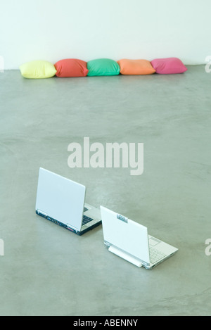 Two laptops on floor, cushions in background Stock Photo