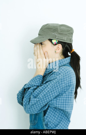 Teen girl wearing overalls and cap, covering face, side view Stock Photo