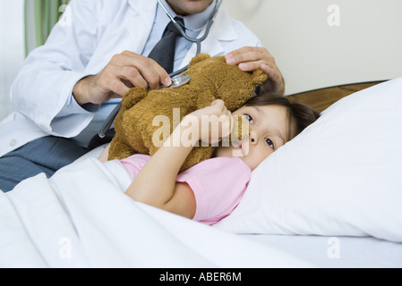 Doctor holding stethoscope to sick child's teddy bear Stock Photo