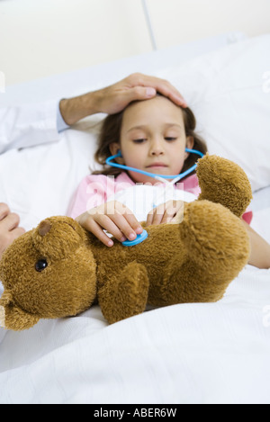 Child holding toy stethoscope to teddy bear, doctor feeling child's forehead Stock Photo