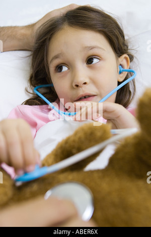 Child holding toy stethoscope to teddy bear, talking to man Stock Photo