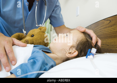 Girl lying in hospital bed, male nurse's hand on girl's head Stock Photo