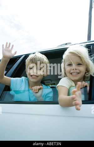 Children sticking heads out of car window, waving Stock Photo