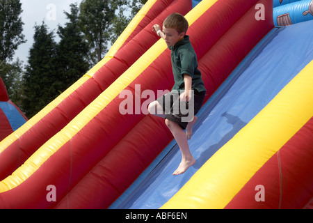 A nine year-old boy cub scout leaps confidently down a slope of an inflatable slide in London, England. Stock Photo