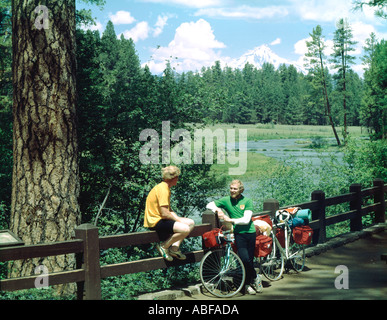 Touring bicycle pair stop for a chat at the Headwaters of the Metolious River in Oregon to enjoy a view of Mount Jefferson Stock Photo