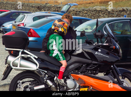 A young boy dressed in football strip and wearing a huge crash helmet sat on a motorcycle talking to the owner Stock Photo