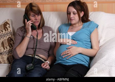 Young heavily pregnant woman with mother/midwife/ relative/neighbour who is phoning for help Stock Photo