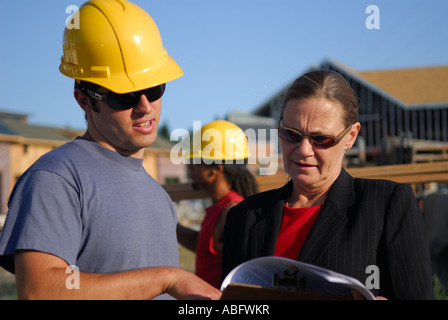 Contractor foreman in hard hat explaining progress to the female architect outdoors at construction site Stock Photo