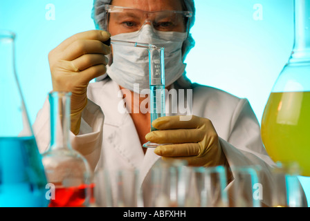 Masked female laboratory technician adding liquid to a graduated cylinder surrounded by colored fluids in flasks Stock Photo