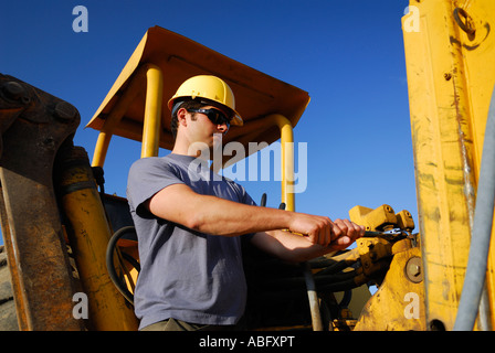 Construction worker in yellow hard hat tightening a connection on a backhoe equipment Stock Photo