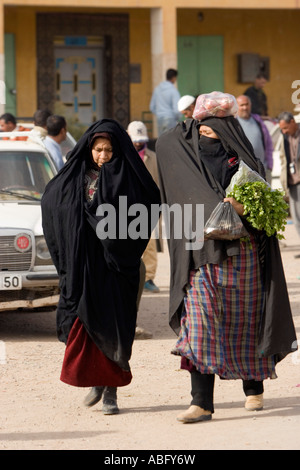 Two women in traditional black robes covering head carry vegetables street market Jorf in Tafilalt Morocco Stock Photo