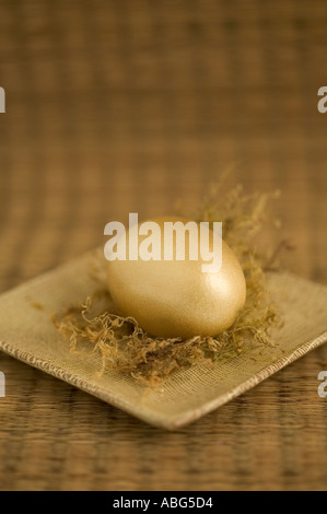 Golden egg sits on square plate in golden brown still life set Stock Photo