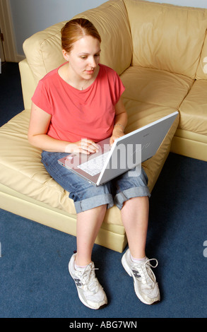 Young woman using Sony Vaio wireless laptop sitting on sofa wearing jeans pink tee shirt and trainers UK Stock Photo