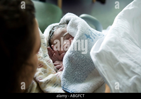 Newborn baby girl is just born at hospital. She is just 10 minutes old, wrapped in towel she is in her mum’s arm. Stock Photo