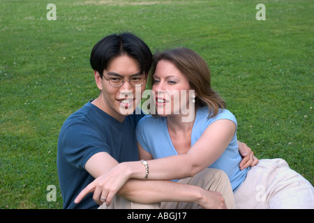 Interracial couple sitting on a lawn in a park Stock Photo