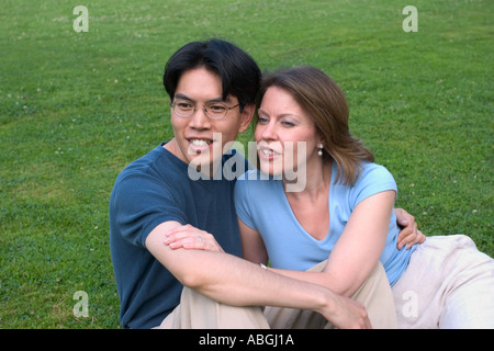 Interracial couple sitting on a lawn in a park Stock Photo