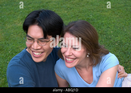 Interracial couple sitting on a lawn in a park Stock Photo