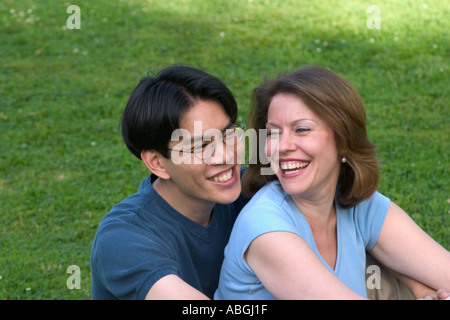 Interracial couple sitting on a lawn in a park Stock Photo