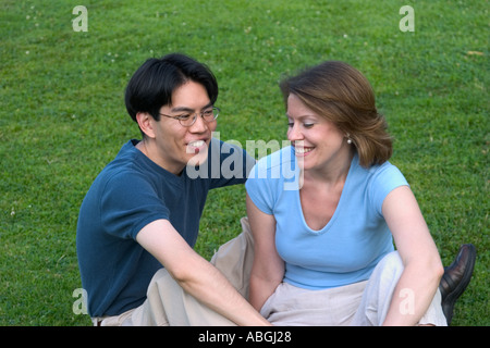 Interracial couple sitting on a lawn in a park Stock Photo